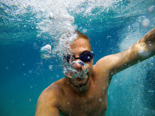 Close up view of young adventuristic bearded man with googles diving in the exotic turquoise sea...