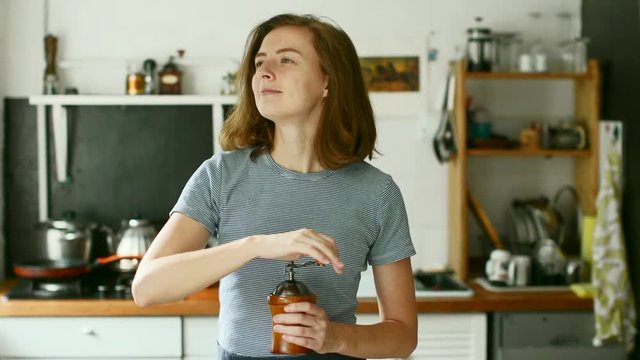 Young woman holding a coffee grinder and making fresh coffee in the kitchen