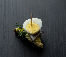 Mini sandwich with salt sprat and sliced boiled quail egg on the slice of bread. Canned fish is...