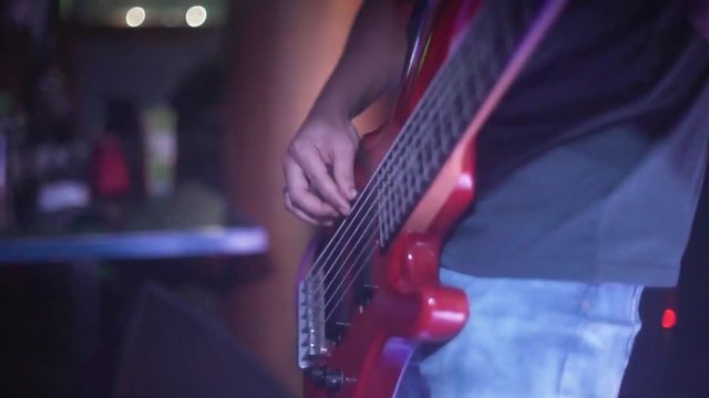 Fast finger picking on red extended six string bass at rock concert.