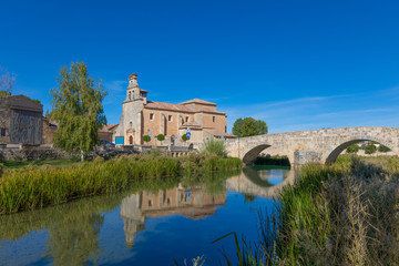 Fototapeta na wymiar church of Santa Cristina and stone roman footbridge, reflected on water of Ucero river, landmark and public monument in Burgo de Osma, Soria, Spain, Europe 