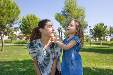 woman talking to four years old blonde girl in green grass of park
