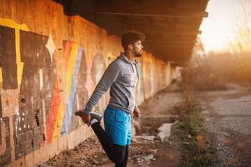 Portrait of focused motivated afro-american young handsome sportive man with earphones standing inside of the abandoned place. Successful young active man portrait.