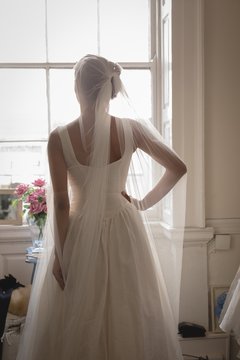Rear view of bride in wedding dress looking out through window