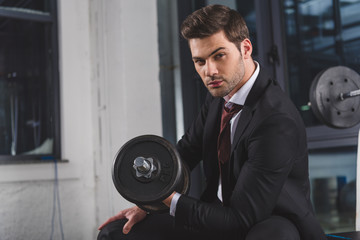 handsome businessman in suit training with dumbbell in sports center