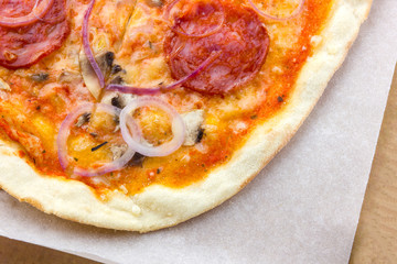 Pizza closeup on the table. Pizza with cheese, tomatoes, onions and spicy sausage salami.