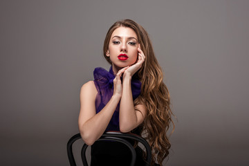 beautiful model in trendy purple scarf posing on chair, isolated on grey