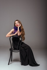 beautiful model in black dress and purple scarf sitting on chair, on grey