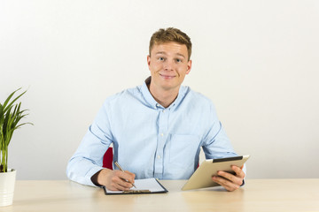 Portrait of a handsome young smiling man using digital tablet by the desk