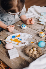 Happy easter! Cute little child girl painting with blue and yellow colors Easter eggs. family preparing for Easter. Hands of a girl with a easter egg. close-up