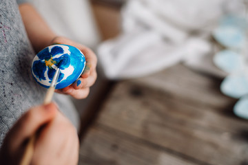 Happy easter! Cute little child girl painting with blue and yellow colors Easter eggs. family preparing for Easter. Hands of a girl with a easter egg. close-up