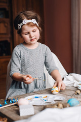 Happy easter! Cute little child girl painting with blue and yellow colors Easter eggs. family preparing for Easter