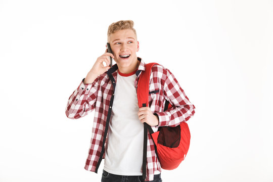 Image of cheerful hipster guy 18y wearing plaid shirt and backpack talking on mobile phone with smile, isolated over white background