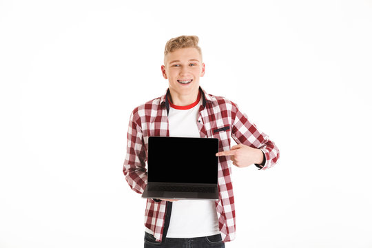 Young hipster man 18y wearing casual shirt holding silver notebook demonstrating or advertising copyspace screen, isolated over white background