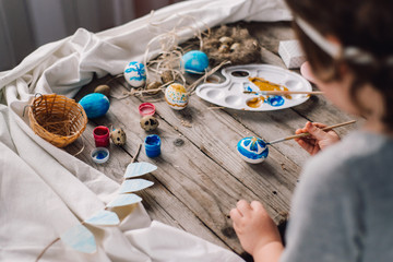 Happy easter! Cute little child girl painting with blue and yellow colors Easter eggs. family preparing for Easter