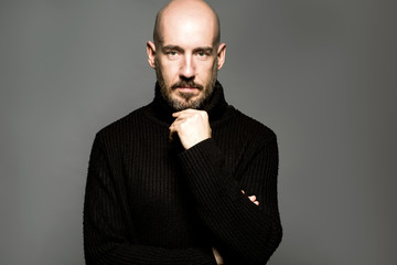 Fashion Portrait man standing over a light gray background in a black sweater. Close up. Classic style. Bald shaved head. Copy-space. Studio shot.