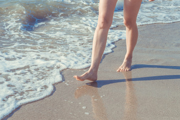 Close up of woman legs walking barefoot on beach in summer holidays. Vacation concept.