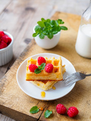 Waffeln mit frischen Himbeeren, Honig, Pfeffermine und eine Flasche Milch auf einem braunen Holztisch. Nahaufnahme, Frühstück, Dessert.