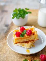 Waffeln mit frischen Himbeeren, Honig, Pfeffermine und eine Flasche Milch auf einem braunen Holztisch. Nahaufnahme, Frühstück, Dessert.