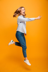 Fototapeta na wymiar Full length image of pleased woman wearing jeans and sneakers smiling and pointing finger aside on copyspace, isolated over yellow background