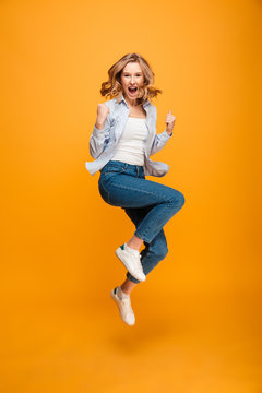 Full length picture of content ecstatic adult girl expressing delight and clenching fists, isolated over yellow background
