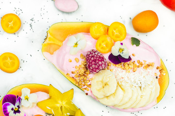 Fototapeta na wymiar Fresh colourful papaya smoothie bowl on marble background, healthy vegan breakfast concept