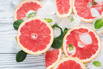 Naklejka na ściany i meble Top view of red grapefruit slices, ice and mint on a white wooden background. The concept of a healthy diet. Detox.