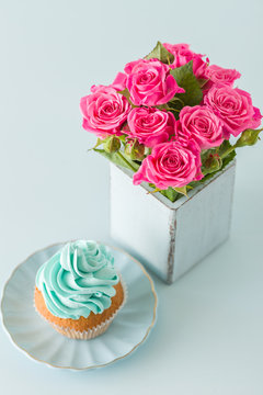 Blue pastel vertical banner with decorated with blue cream cupcake and pink roses in retro shabby chic vase.