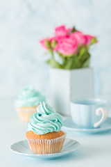 Blue pastel vertical banner with decorated cupcakes, cup of coffe with milk and bouquet of pink roses.