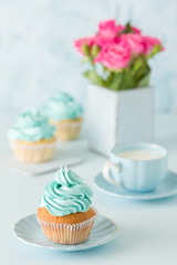 Blue pastel vertical banner with decorated cupcakes, cup of coffe with milk and bouquet of pink roses.