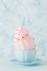 Cupcake with gentle pink cream decoration in two cups on blue pastel background.