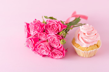Cupcake with pink cream decoration and roses on pink pastel background.