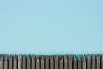 Row of metal bits for screwdriver in form of triangle on blue background with copy space