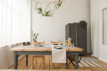 Cozy interior of kitchen with wooden table and cupboard and green plants in decor. 