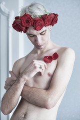 Beautiful aesthetic guy with red flowers on his head and red petals