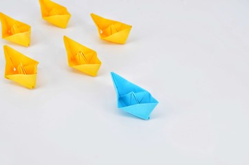 Leadership concept with a blue paper ship leading among yellow ships.