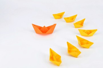 Leadership concept with a orange paper ship leading among yellow ships.