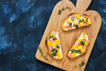 Toast with ham jamon avocado and cream cheese on a cutting board, blue fashioned rustic background, top view.