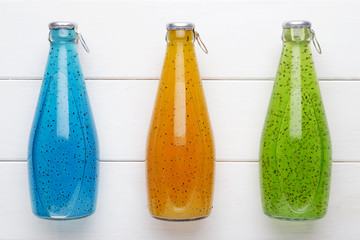 Colorful drinks in three bottles on white wooden table.