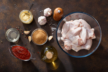 Fototapeta na wymiar Fresh raw chicken wings and ingredients for bbq sauce on brown rusty background.