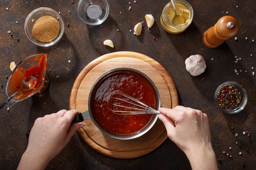 Hands mix the bbq sauce with the whisk in the saucepan. - 197516454