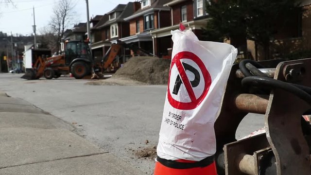 No Parking pilon with construction digger in the back ground. Spring time road and home repair. Road closed due to construction.