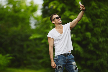 Stylish handsome young athletic men, in white t-shirt and jeans, make a selfie on his smartphone