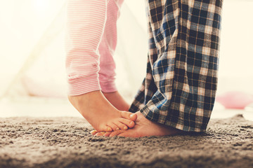 Family relationships. Close up of a cute nice small girl standing on the fathers feet while being...