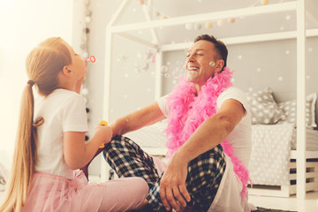 Fun activity. Happy pretty delighted girl blowing soap bubbles and laughing while having fun with her father