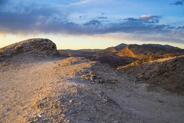 A rocky ridge and mountains lit up at golden hour under a partially cloudy sky