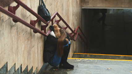 Young girl on the stairs in the subway depressed sitting alone obscures the face with his handsand crying. Autumn.