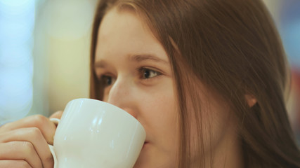 Close-up face of young beautiful schoolgirl, drinking coffee from a cup.