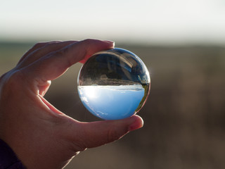 Woman hand holding glass ball with panoramic view of countryside and sky/ Concept for environment