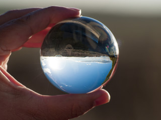 Woman hand holding glass ball with panoramic view of countryside and sky/ Concept for environment